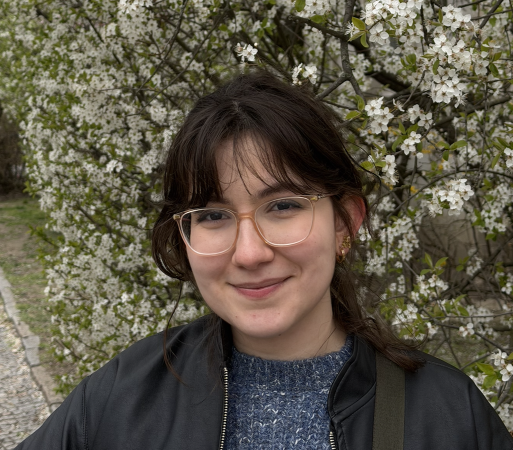 Luísa de Souza Ferreira, with long red hair and brown eyes, wearing glasses, walking on the street with Manhattan Bridge in the background.